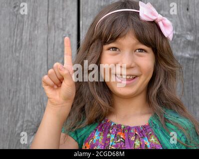 Cute mixed-race little girl (East Asian / Caucasian) shows with her right hand the Chinese hand sign for number 1 (photo series: image no. 1 of 10). Stock Photo