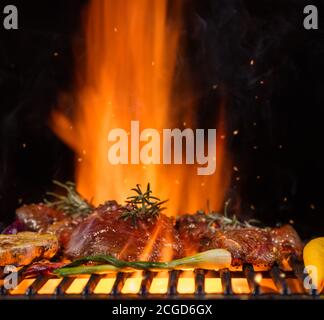 Beef steaks with vegetable on the grill grate, flames on background. Barbecue and grill, delicious food. Stock Photo