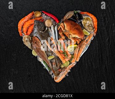Fresh seafood, mussels, prawns, fish, crab, salmon steak, mackerel and other shells in heart shape. Served on black stone. Concept of seafood and love Stock Photo