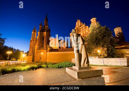 Night view of illuminated Mickiewicz statue at Maironio Street in the Old Town of Vilnius, Lithuania. Gothic style St. Anne Church and St. Francis and Stock Photo