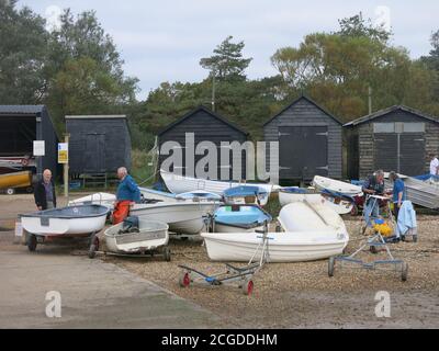 A row of black sheds with small boats in the foreground at Orford Quay, a small boating and fishing community in Suffolk. Stock Photo