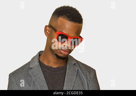 African American man in smart casual clothes and and sunglasses looking down against gray background Stock Photo