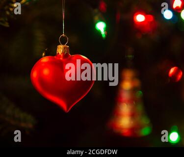 Heart shaped glass Christmas ornament hanging in an illuminated balsam fir Christmas tree. Stock Photo