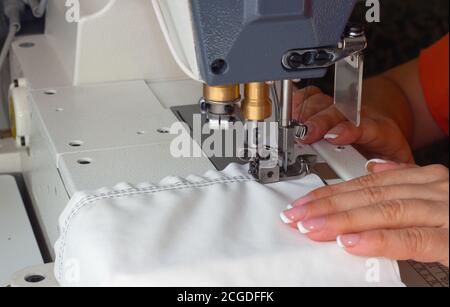 A woman sews on an industrial flat-seam sewing machine. Hands close-up. Soft focus Stock Photo