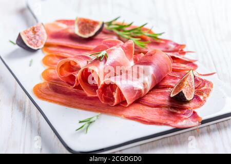 Delicious Serrano ham with fresh figs and rosemary on white cutting board Stock Photo