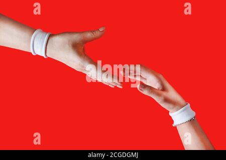 Giving a helping hand. Helping hand to a friend. Hands with white bracelets on red backgroung. Stock Photo