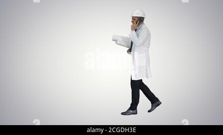 Successful architect is talking on the mobile phone and walking on gradient background. Stock Photo