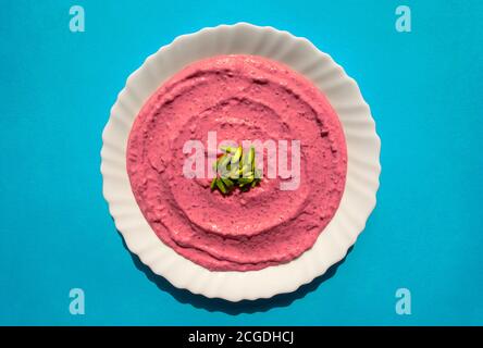 Famous traditional Arabic cuisine - Beet hummus in a white plate on blue background. Arabic beet and pomegranate labneh or yogurt. Top view Stock Photo