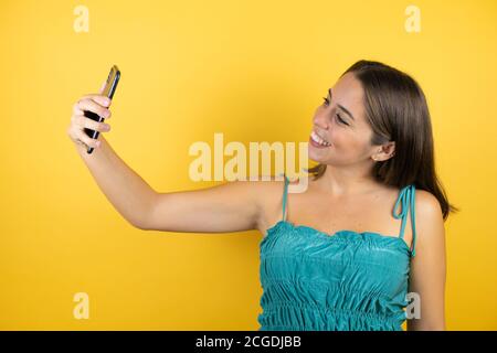 Young beautiful woman over isolated yellow background taking a selfie with her phone Stock Photo