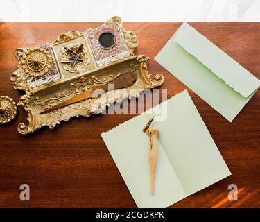 Brass inkwell on wood desk with mint green stationary envelope and pen Stock Photo
