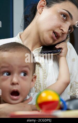 Mommy talking on the phone. Working from home due to coronavirus. A young middle-eastern woman trying to work at home while sitting with her baby boy Stock Photo