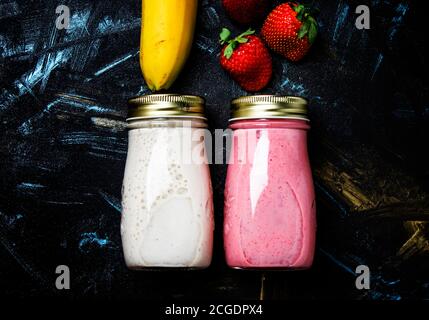 Food background, smoothies from strawberries and banana in small bottles, dark background, top view, flat lay Stock Photo