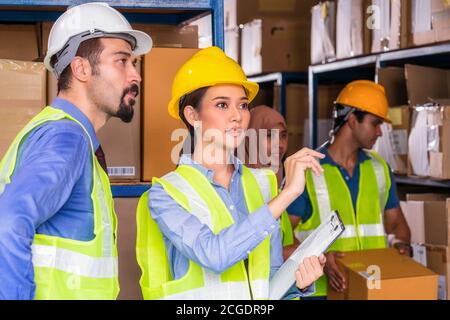 Asian assistant manager woman reporting to White Caucasian Manager of warehouse worker with Muslim and Indian worker working in local warehouse,Divers Stock Photo