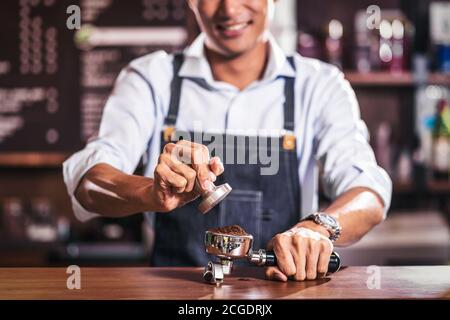 Asian Barista tamping the portafilter and preparing cup of coffee, espresso with latte or cappuccino for customer order in coffee shop, Small business Stock Photo