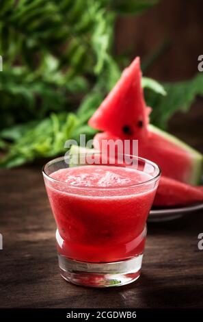 Freshly squeezed watermelon smoothie in glass and slices of watermelon on old wooden kitchen table background Stock Photo