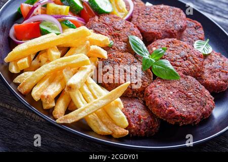French fry, fresh salad of tomato cucumber and red onion with fresh basil served with beetroot patties of mushrooms and black beans on a black plate o Stock Photo