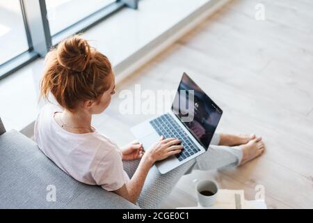 Image of focused redhead woman working with laptop while sitting on floor at home Stock Photo
