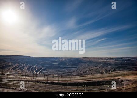 Open pit extraction of coal in quarry 'Bogatyr', Ekibastuz, Kazakhstan. Quarry truck, excavators and train. Wide-angle panorama. Blue sky with clouds. Stock Photo