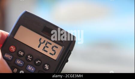 Calculator with YES on display on blue blured background. Positive thinking concept Stock Photo