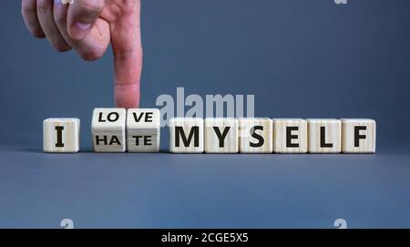 Hand turns cubes and changes the expression 'I hate myself' to 'I love myself'. Beautiful grey background, copy space. Concept. Stock Photo