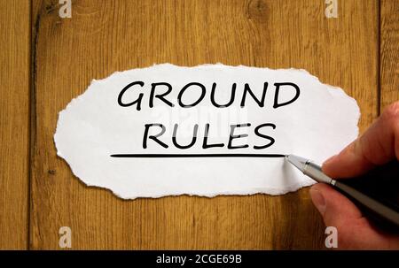 Male hand writing 'ground rules' on white paper on wooden table. Business concept. Stock Photo