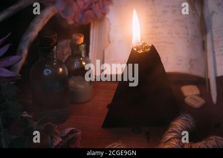 Open old book with magic spells, runes, black candle and herbs on witch table. Occult, esoteric, divination and wicca concept. Halloween vintage backg Stock Photo