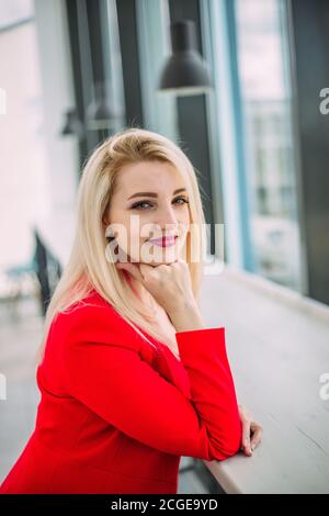 Attractive successful business lady in a red suit in a light office building by the window Stock Photo