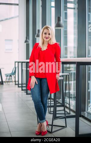 Attractive successful business lady in a red suit in a light office building by the window Stock Photo