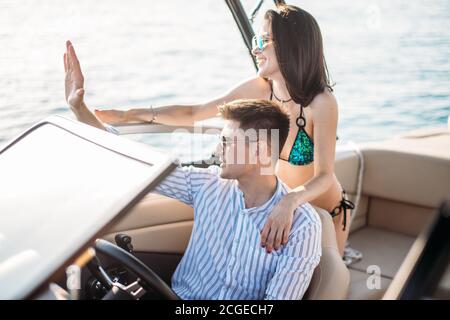 Newly married caucasian couple driving sailboat, enjoying water summer adventure, spending honeymoon in the sea cruise, romantic relationship, happy y Stock Photo