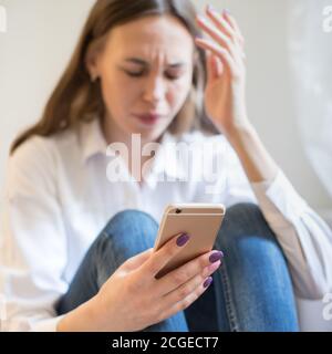Crying woman in depression looking at phone gets bad news, sitting, focus on smartphone. Stock Photo