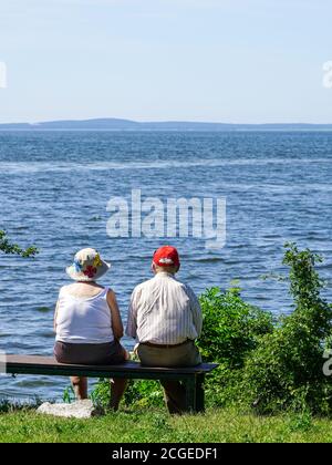 old woman and man sitting on a bench by the sea and looking into the distance, rear view Stock Photo