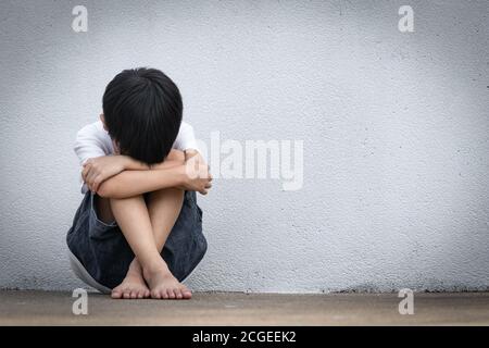 A boy sitting alone with sad feeling. Asian little child covered his face with his hands in fear.  Domestic Family violence concept. Stock Photo