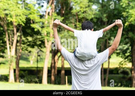 Dad giving son ride on back in the park. Asian family cute and warm. Father and child having fun outdoors. Stock Photo