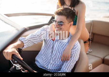 Wealthy succsessful businessman rent a speed luxury motor boat to take a drive with his new passion- young pretty girl with good slim body dressed in Stock Photo