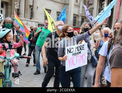 Woman protester wearing a facemask holds placard reading 'No more fashion victims' during the protest.Extinction Rebellion demonstrators march to Westminster as part of their Redress the Injustice day of protest, opposing the fashion industry’s many human, animal and environmental injustices. Stock Photo