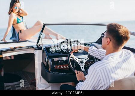 Newly married caucasian couple driving sailboat, enjoying water summer adventure, spending honeymoon in the sea cruise, romantic relationship, happy y Stock Photo