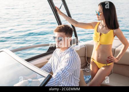 Cute married couple having their honeymoon trip on a luxury sailing boat at summer Carribean Sea. Husband sitting at steering wheel and his loving you Stock Photo