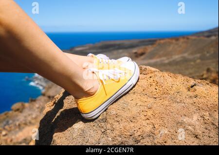 Close up view, of woman feet wearing sneakers . Traveler Sitting On Rock wearing yellow sneakers. Enjoying Summer Vacation.  Stock Photo