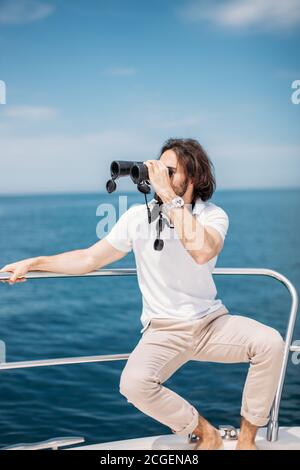 Caucasian Bearded Traveller Man looking through binoculars from the boat, adoring beauty and power of the Ocean Stock Photo