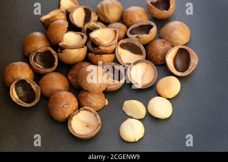 Macadamia nut shell on black background. Raw macadamia nuts and brown shells. Stock Photo
