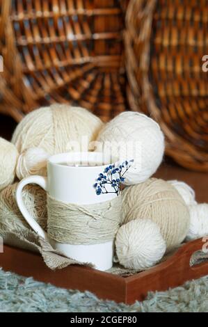 white Cup decorated with twine rope and blue dried flower and white wool threads different sizes balls on wooden tray. cozy warm tea party, vertical Stock Photo