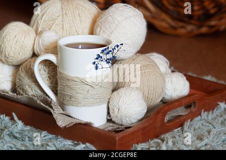 white Cup decorated with twine rope and blue dried flower and white wool threads different sizes balls on wooden tray. cozy warm tea party, selective Stock Photo