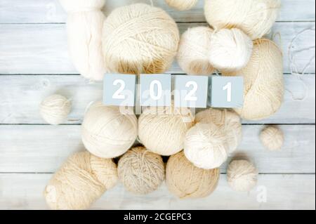 gray wooden cubes with the numbers 2021 and a lot of light wool balls of knitting thread, top view, selective focus Stock Photo