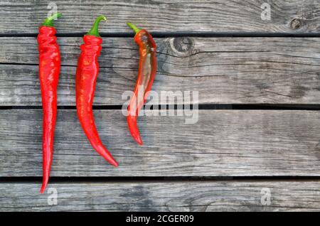 Three red hot chili peppers on an old wooden table as a background. Close-up, top view Stock Photo