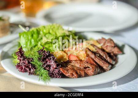 Roasted meat with garnish and fresh lettuce leaves on a white plate. Close-up, selective focus Stock Photo