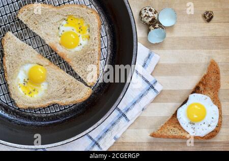 Slices of bread with fried quail eggs in a frying pan placed on a wooden cutting board as a background, top view. Healthy eating concept. Stock Photo