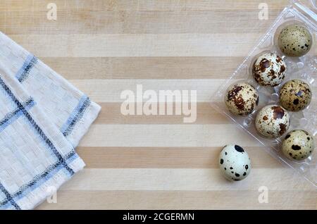 Speckled quail eggs in a plastic transparent tray on a wooden cutting board with a kitchen towel close-up with copy space, top view. Healthy eating Stock Photo