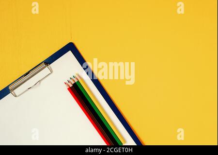 A paper tablet with a blank sheet and five colored wooden pencils on a bright yellow wooden background Stock Photo