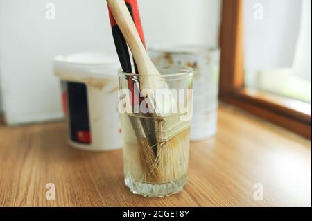 tools for home self-repair. wall paint brushes soaked in water, blurred cans of paint on the background stand on a wooden window in the room Stock Photo