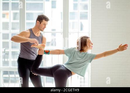 Professional Yoga male instructor helps female beginner to make asana  against big window in light sunny studio. Master assisting his pupil to  make yog Stock Photo - Alamy